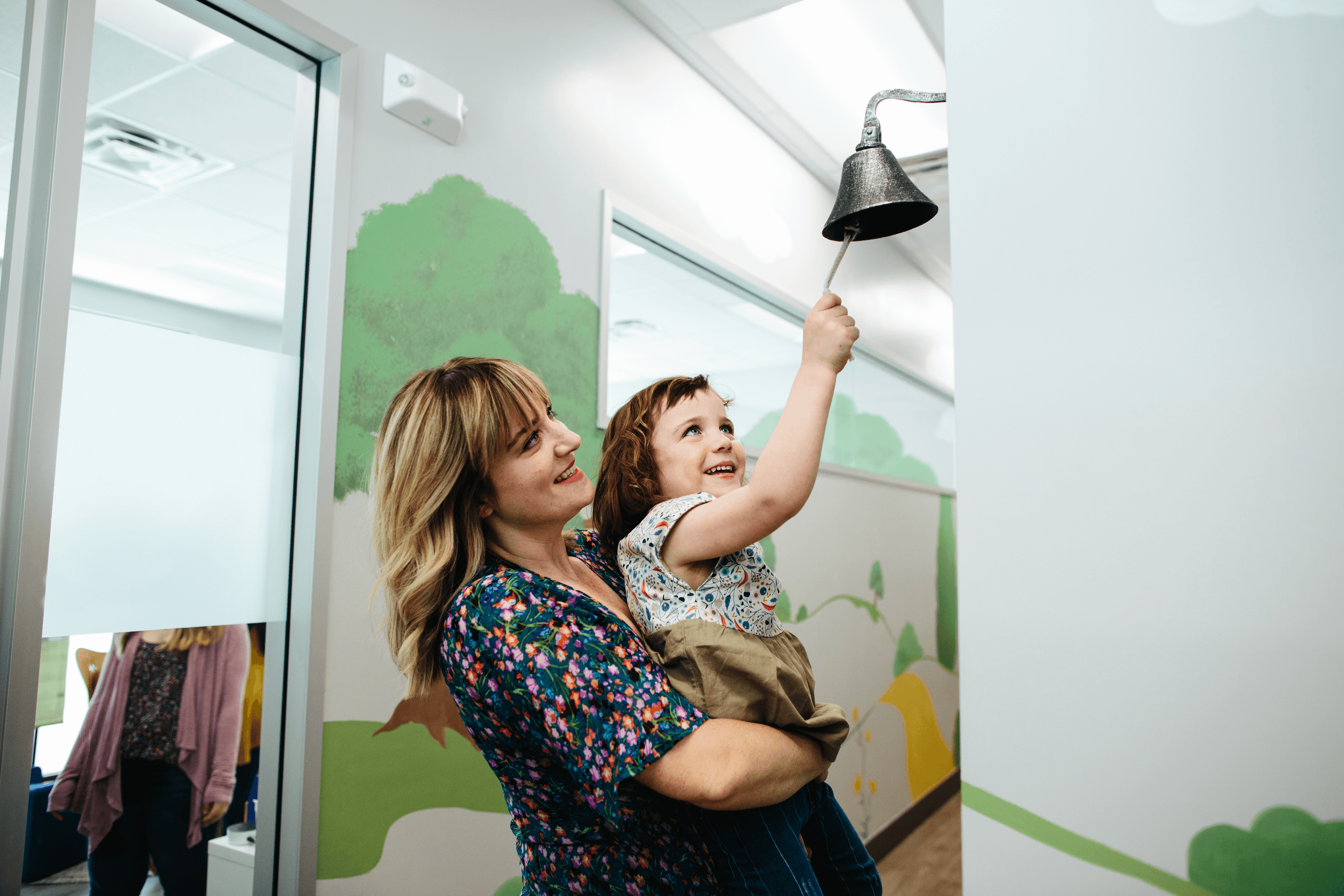 A woman holding a child who is ringing a bell