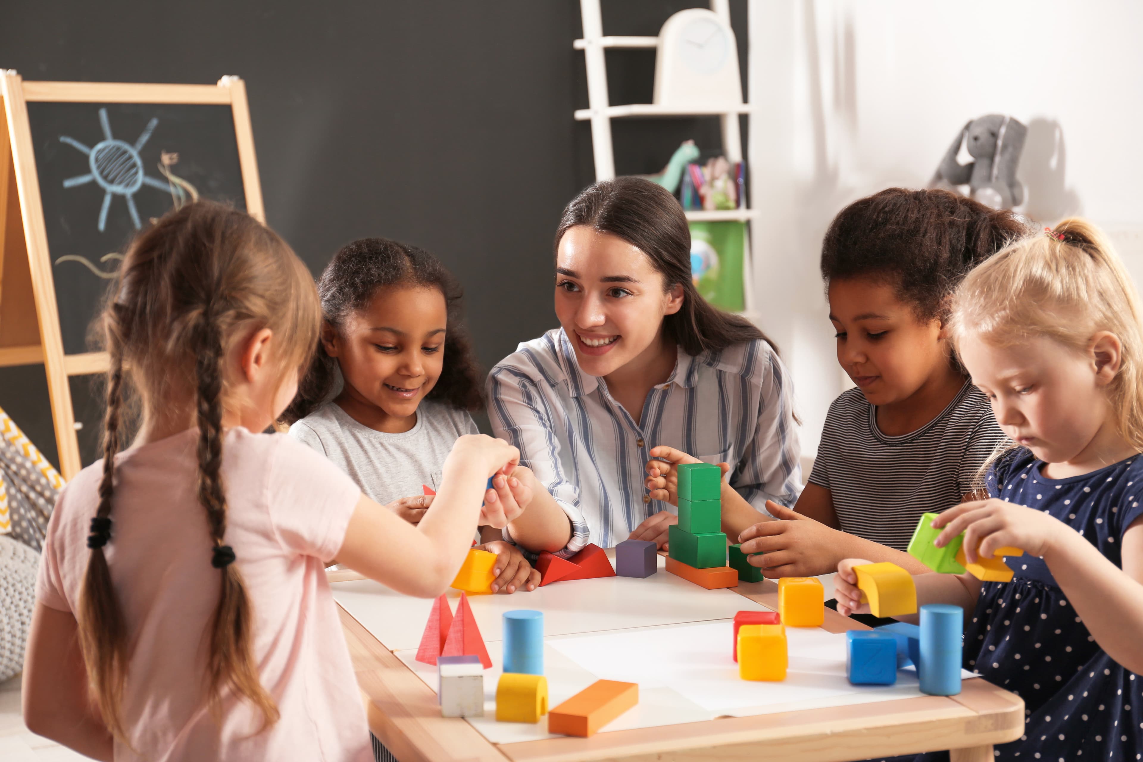 An adult and four children playing with blocks at a table