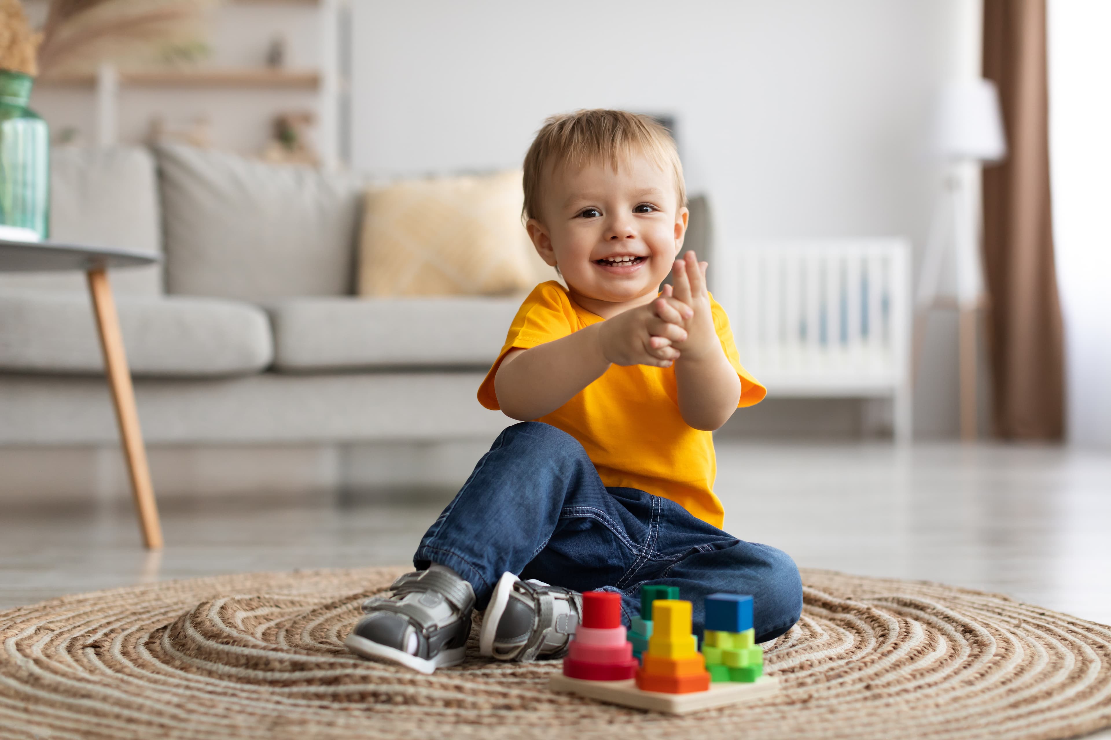 A smiling toddler on a mat playing with colorful blocks