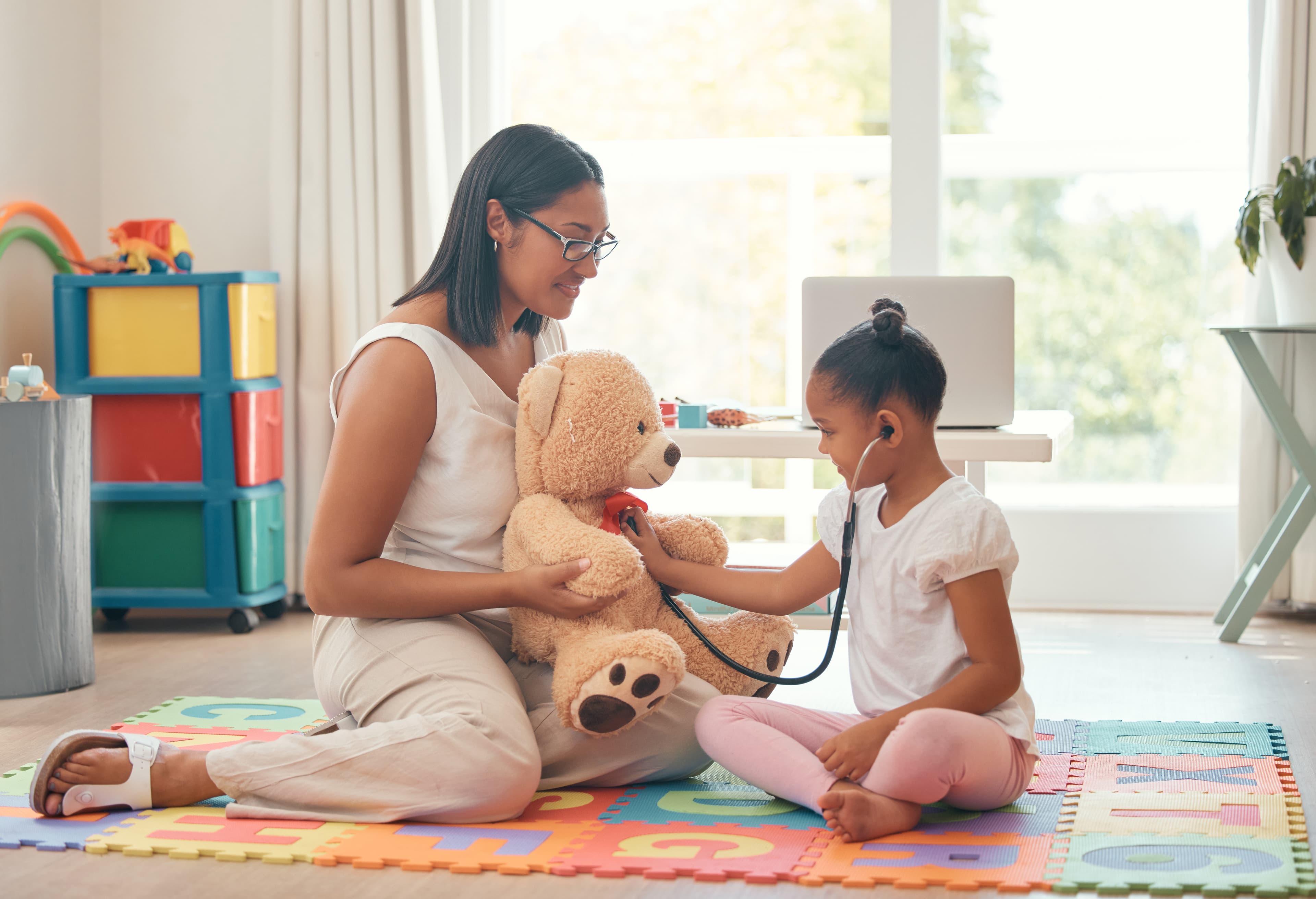 A child wearing a stethescope and listening to a teddy bear's heart