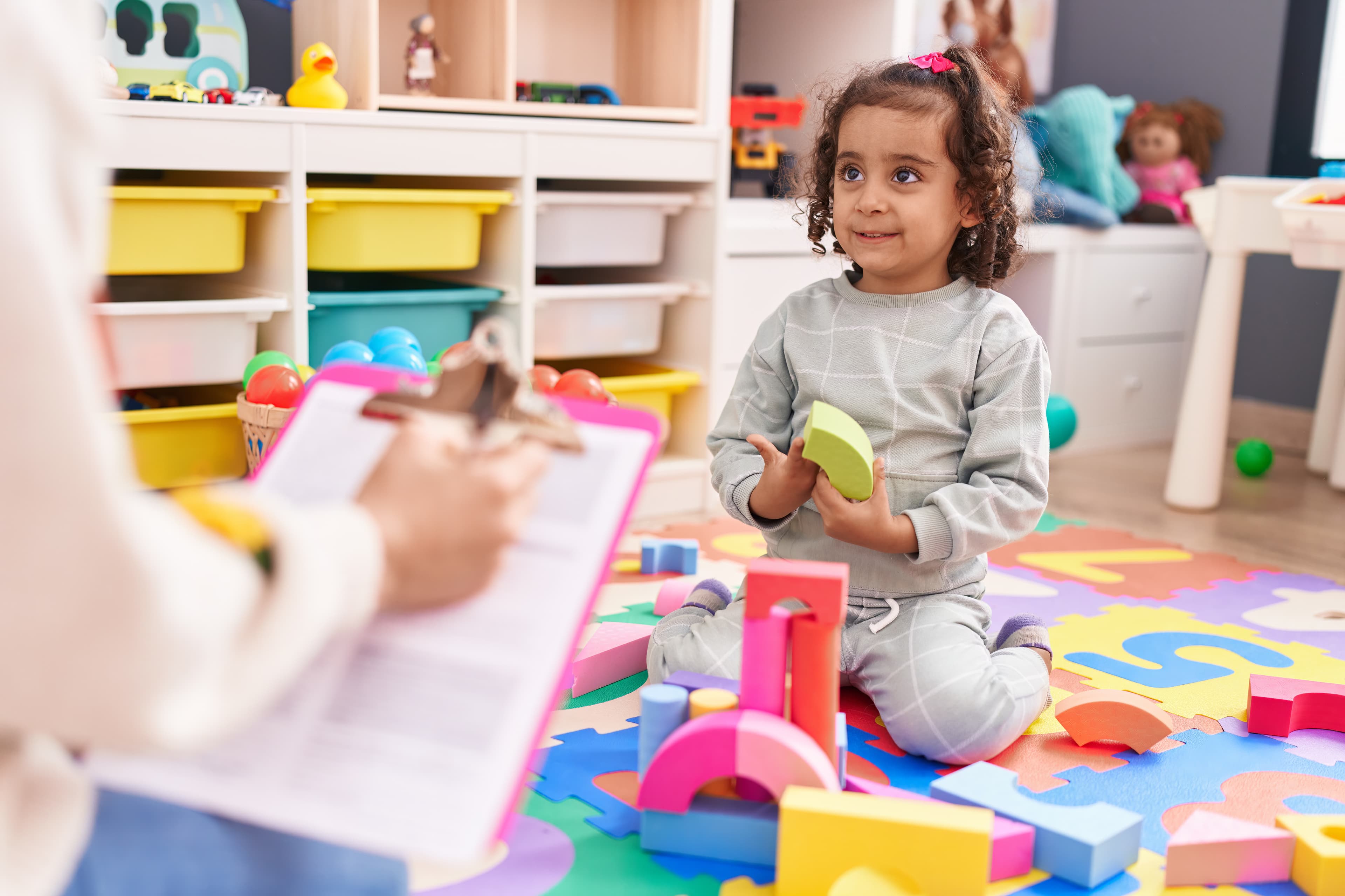 A toddler playing with toy blocks on a colorful mat