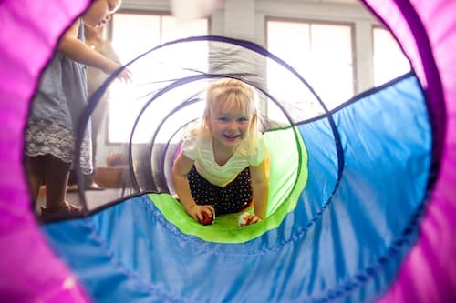 A smiling toddler crawling through a tunnel