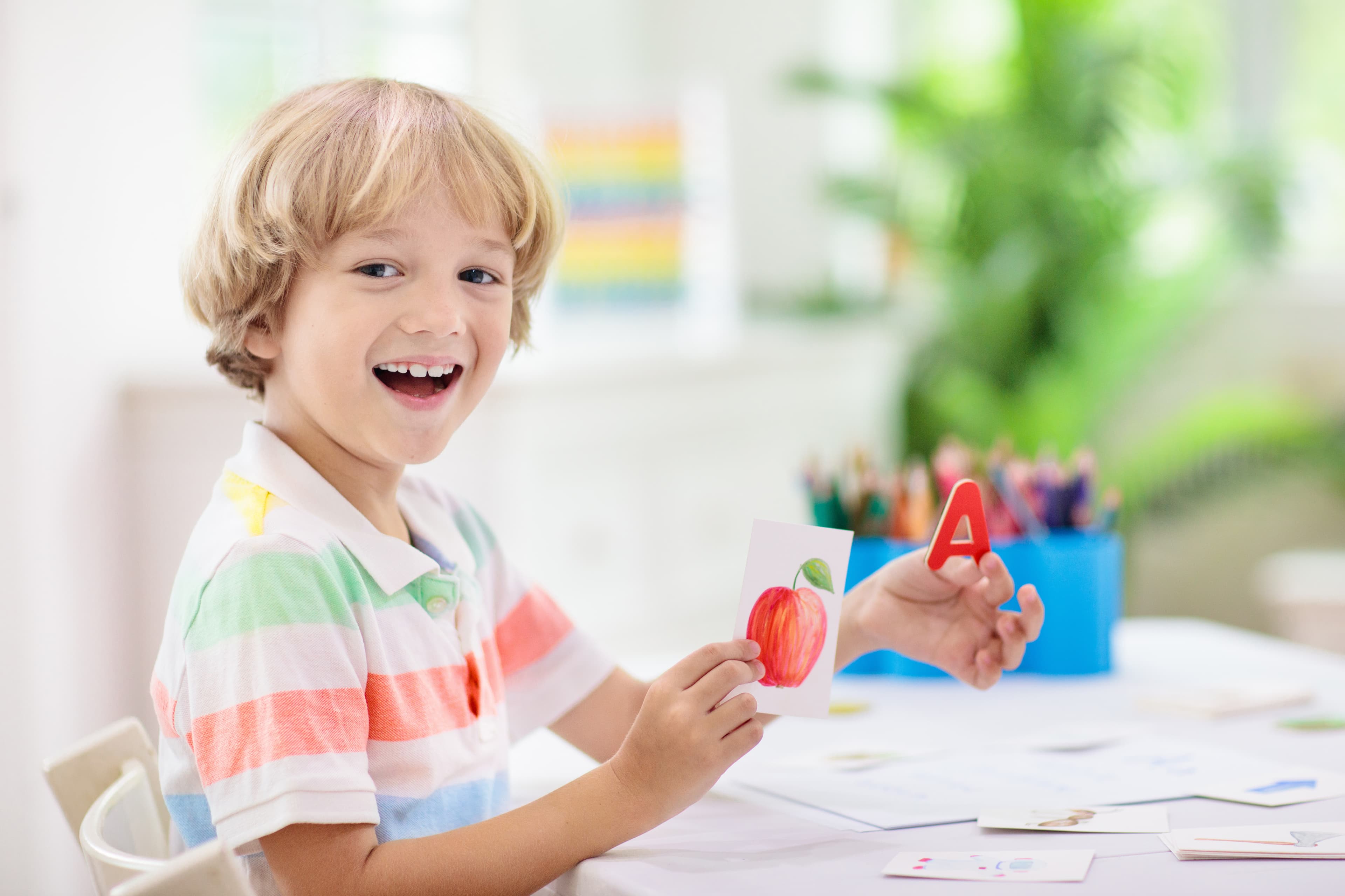 A smiling child holding up a flashcard with an apple on it.