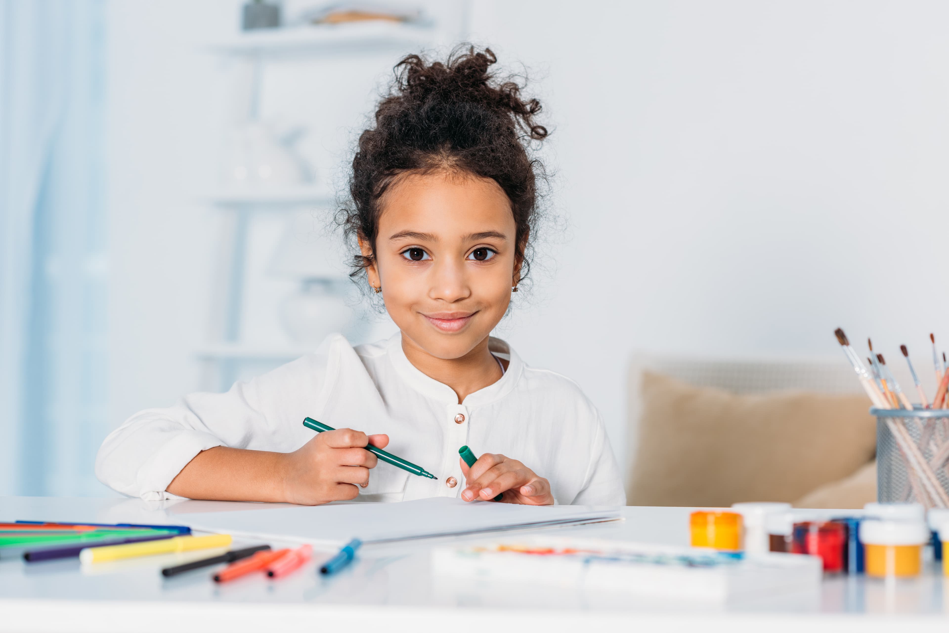 A smiling girl sitting at a table with a green pen