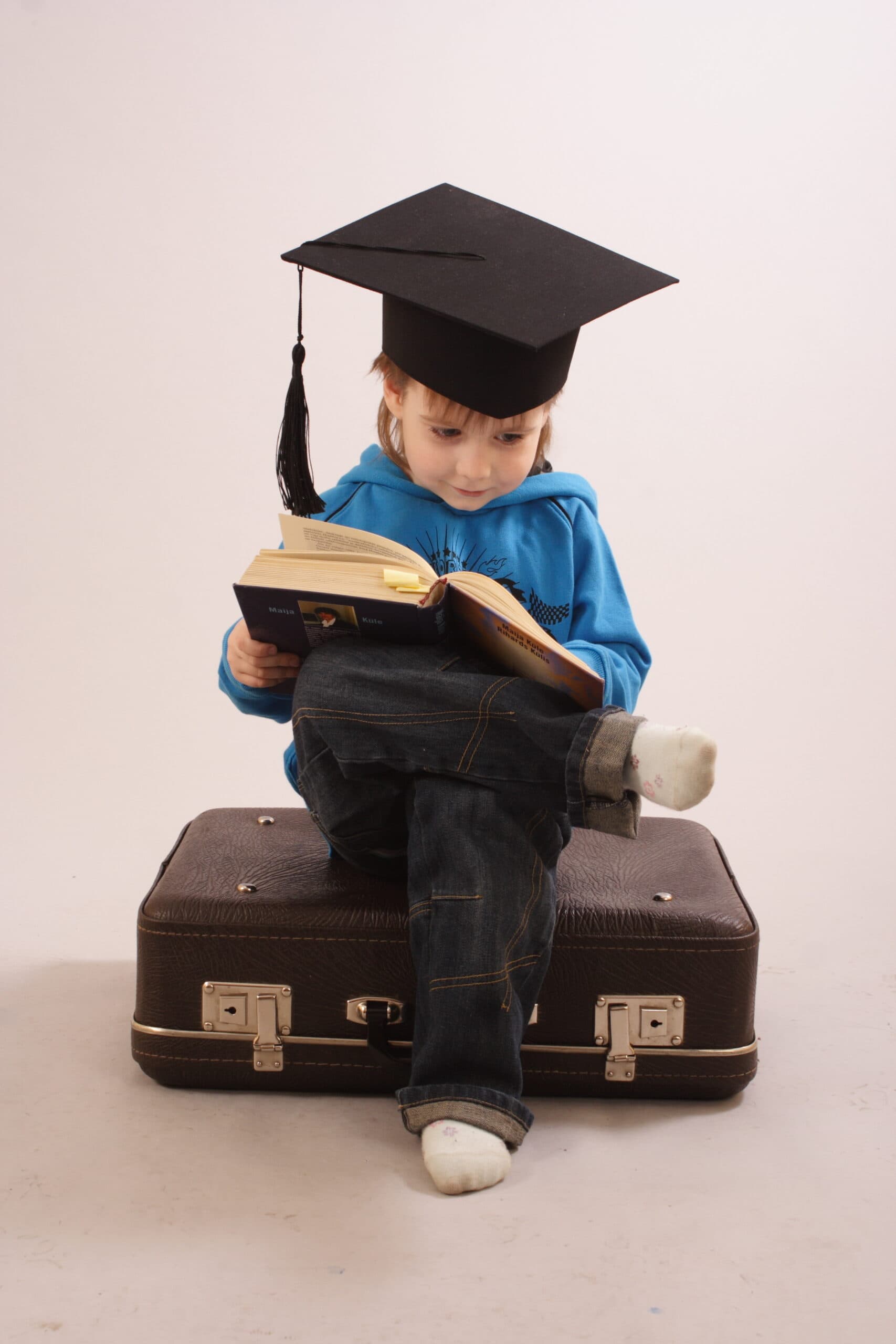 Toddler wearing graduation cap sitting and reading