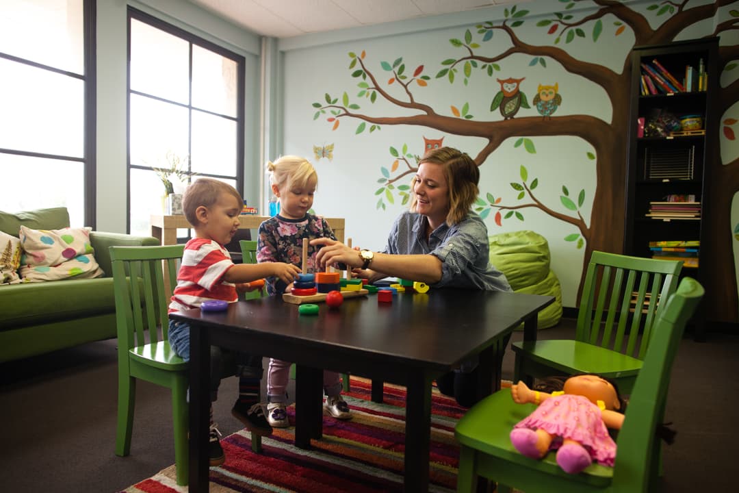 An adult and two toddler playing with blocks on a table